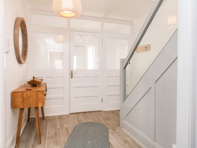 An entryway with a wooden side table a round mirror on the wall a rug on the floor and a staircase with a glass panel at Greenbank in Woolacombe