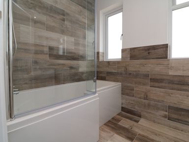 A bathroom with a bathtub shower combination and wood effect tiles on walls and floor at Greenbank in Woolacombe