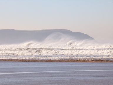 Waves crashing on a beach with a hill in the background at Greenbank Woolacombe