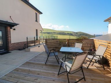 An outdoor patio with four chairs and a glass table with a wooden fence and hills in the background at Greenbank in Woolacombe