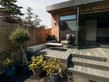 An outdoor wooden deck with two chairs a table and potted plants at Nightingales in Bridlington