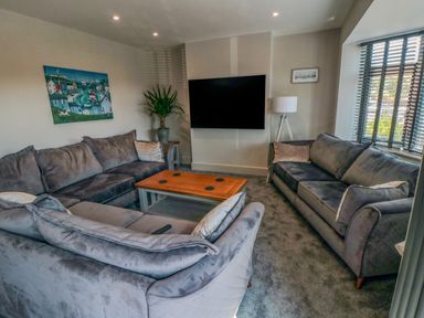 A living room with two grey sofas a wooden coffee table a wall-mounted TV a floor lamp a potted plant and a painting on the wall at Nightingales in Bridlington