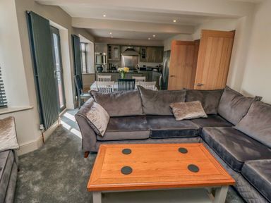 A living room with a grey sectional sofa a wooden coffee table and an open doorway to a kitchen with a dining table and chairs at Nightingales in Bridlington