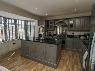 A kitchen with gray cabinets black countertops an island and large windows with blinds at Nightingales Bridlington