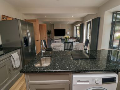 A kitchen with a black countertop island featuring a sink and washing machine a dining table with chairs and a living area with a television at Nightingales in Bridlington