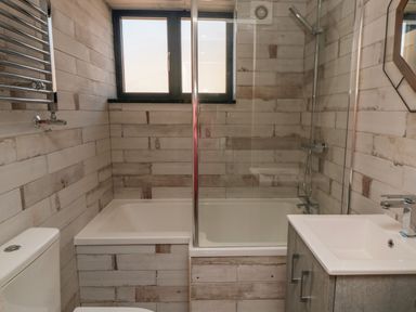 A bathroom with a bathtub shower combination a toilet a sink with vanity and a window at Nightingales in Bridlington