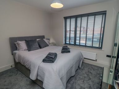 A bedroom with a bed with pillows and folded towels on top next to a window with blinds at Nightingales in Bridlington
