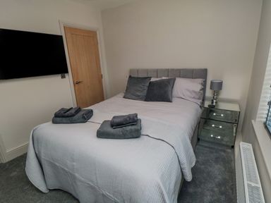 A bedroom with a double bed grey bedding towels on bed mirrored bedside table lamp wall mounted television a nightingales bridgington