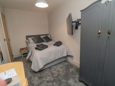 A small bedroom with a double bed grey pillows a wall-mounted tv a grey wardrobe and a bedside table at Nightingales in Bridlington