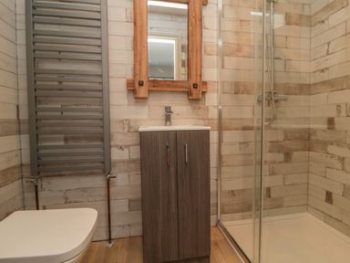 A bathroom with a toilet, gray towel radiator, wooden vanity with sink, mirror, and glass shower enclosure at Nightingales in Bridlington