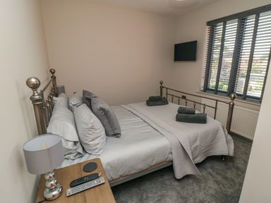 A bedroom with a metal bed frame pillows and folded towels on the bed a bedside table with a lamp and remote controls and a window with blinds at Nightingales in Bridlington