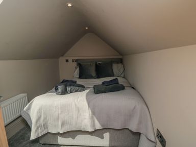 A small bedroom with a double bed towels on the bed and slanted ceiling at Nightingales in Bridlington
