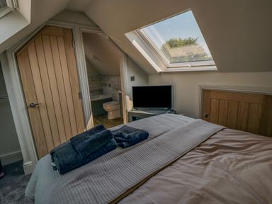 A bedroom with a bed towels a television a skylight window and an en suite bathroom at Nightingales in Bridlington