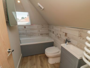 A small bathroom with a bathtub toilet and sink under a slanted ceiling at Nightingales in Bridlington