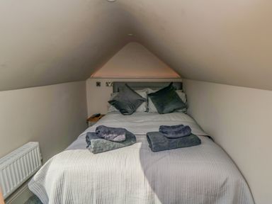 A small bedroom with a bed placed under a sloped ceiling with pillows and folded towels on the bed at Nightingales in Bridlington