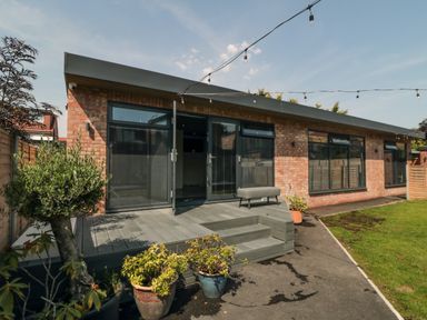 A backyard with potted plants patio steps and a brick house with black framed windows and doors at Nightingales in Bridlington