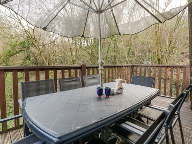 An outdoor patio table with six chairs under a large umbrella with a teapot and two cups on the table at Hideaway Cottage in St Ann's Chapel Cornwall
