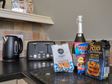 A kitchen with a kettle, toaster, sparkling wine, candy, and cookies at Hideaway Cottage St Ann's Chapel, Cornwall