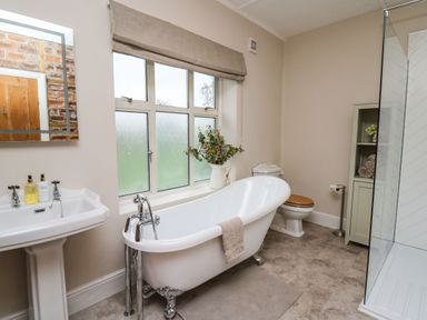 A bathroom with a freestanding bathtub a pedestal sink a toilet a glass shower enclosure and a storage cabinet with towels and flowers at Tirallen in Llangadog