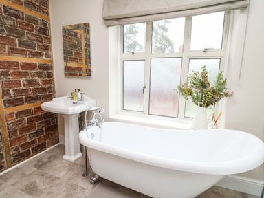 A bathroom with a white freestanding bathtub and pedestal sink next to a window and brick accent wall at Tirallen in Llangadog