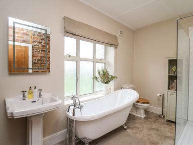 A bathroom with a freestanding bathtub pedestal sink toilet and storage cabinet at Tirallen in Llangadog