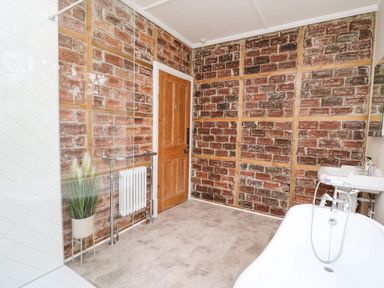 A bathroom with exposed brick walls a wooden door a radiator a white freestanding bathtub and a sink with a mirror at Tirallen in Llangadog