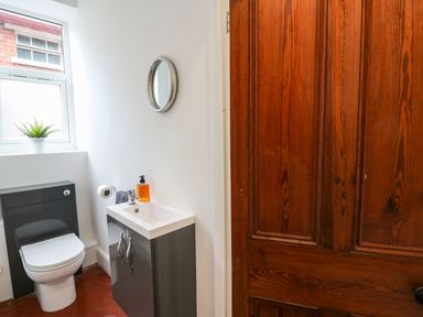 A bathroom with a toilet a sink cabinet a round mirror and a wooden door at Tirallen in Llangadog