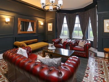 A sitting room with red leather sofas yellow bench mirror and large windows at Tirallen in Llangadog