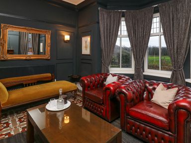 A sitting room with red leather armchairs a mustard sofa a wooden table and a large mirror at Tirallen in Llangadog