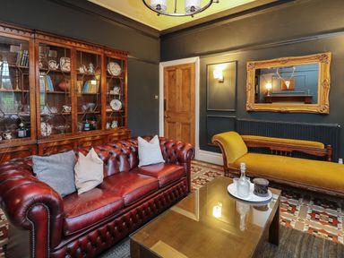 A sitting room with a red leather sofa yellow chaise lounge wooden cabinet and a glass coffee table at Tirallen in Llangadog