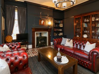 A living room with red leather sofas a fireplace a wooden cabinet and a glass coffee table at Tirallen in Llangadog