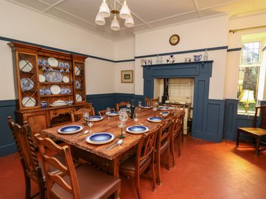 A dining room with a wooden table set with plates glasses and cutlery a wooden cupboard with blue and white dishes and a fireplace with ceramic pitchers at Tirallen in Llangadog