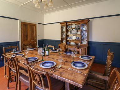 A dining room with a wooden table set with blue plates and glassware and a wooden cabinet with dishes at Tirallen in Llangadog