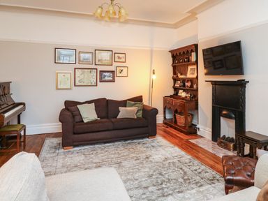 A living room with a dark sofa and cushions a piano wooden cabinet a wall-mounted television and a fireplace at Tirallen in Llangadog