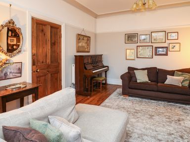 A living room with two sofas a piano wooden door framed pictures and a wooden table at Tirallen in Llangadog