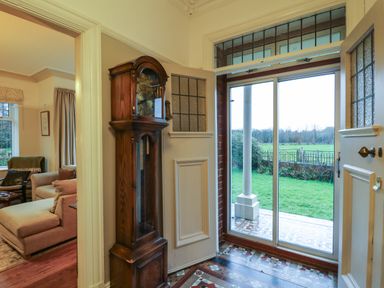 An entryway with a wooden grandfather clock next to an open door with stained glass windows and a sliding glass door showing a green lawn outside at Tirallen in Llangadog