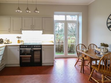 A kitchen with white cabinets a black stove a wooden dining table with chairs and glass doors to the outside at Tirallen in Llangadog