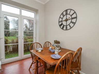 A dining area with a wooden table and four chairs set with plates mugs and a teapot next to glass doors with a garden view at Tirallen in Llangadog