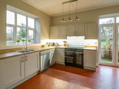 A kitchen with white cabinets wooden countertops stainless steel dishwasher black stove and windows at Tirallen in Llangadog