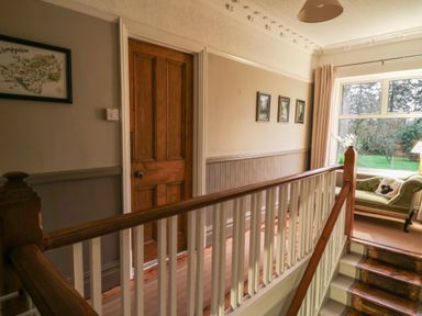 A hallway with a wooden door three framed pictures a window with curtains and a green sofa with a pillow at Tirallen in Llangadog