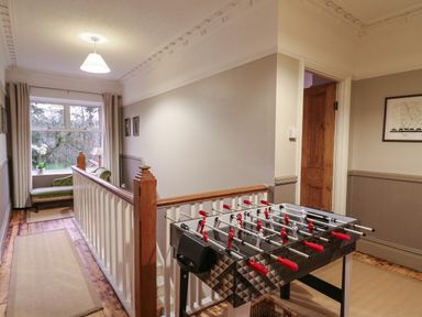 A hallway with a foosball table near a wooden railing and a green chaise lounge by a window at Tirallen in Llangadog