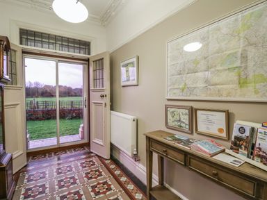 An entryway with an open door leading outside a wooden table with brochures and framed maps on the wall at Tirallen in Llangadog