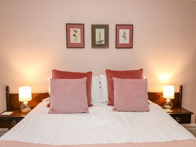 A bedroom with a double bed with pink and red pillows and two bedside tables with lamps at Tirallen in Llangadog