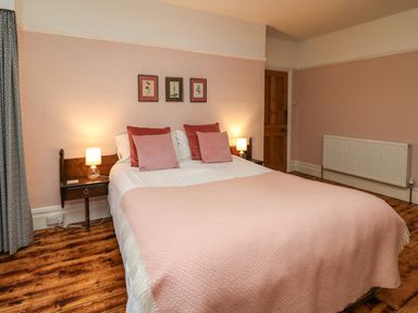 A bedroom with a bed with pink and red pillows and a pink blanket two bedside tables with lamps wooden floor and a wooden door at Tirallen in Llangadog