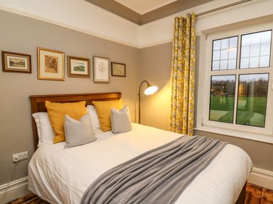 A bedroom with a bed with yellow and gray pillows a gray blanket a floor lamp yellow patterned curtains and framed pictures on the wall at Tirallen in Llangadog
