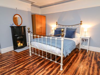A bedroom with a white metal bed with blue pillows and blanket two bedside tables with lamps a wooden wardrobe and a black fireplace at Tirallen in Llangadog