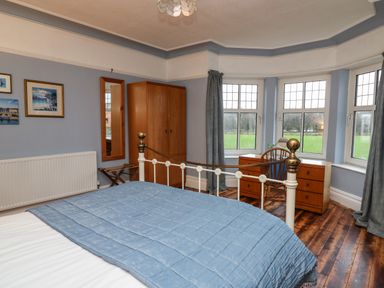 A bedroom with a bed covered by a blue bedspread wooden wardrobe wooden chest of drawers wooden chair and windows with curtains at Tirallen in Llangadog