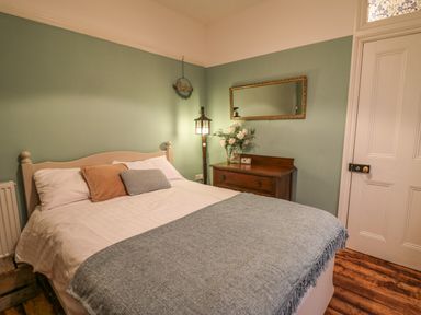 A bedroom with a bed a wooden chest with flowers a wall mirror and a door at Tirallen in Llangadog