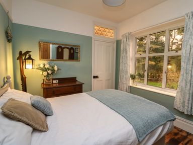 A bedroom with a bed pillows a wooden dresser a mirror and a window with curtains at Tirallen in Llangadog