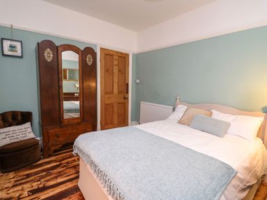 A bedroom with a double bed a wooden wardrobe a closed wooden door and a brown chair with a cushion at Tirallen in Llangadog